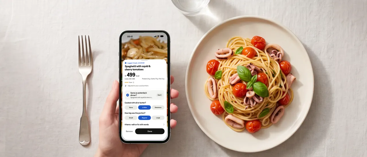 A hand holding an iPhone with Platelight's estimate, beside a plate of spaghetti with squid and cherry tomatoes